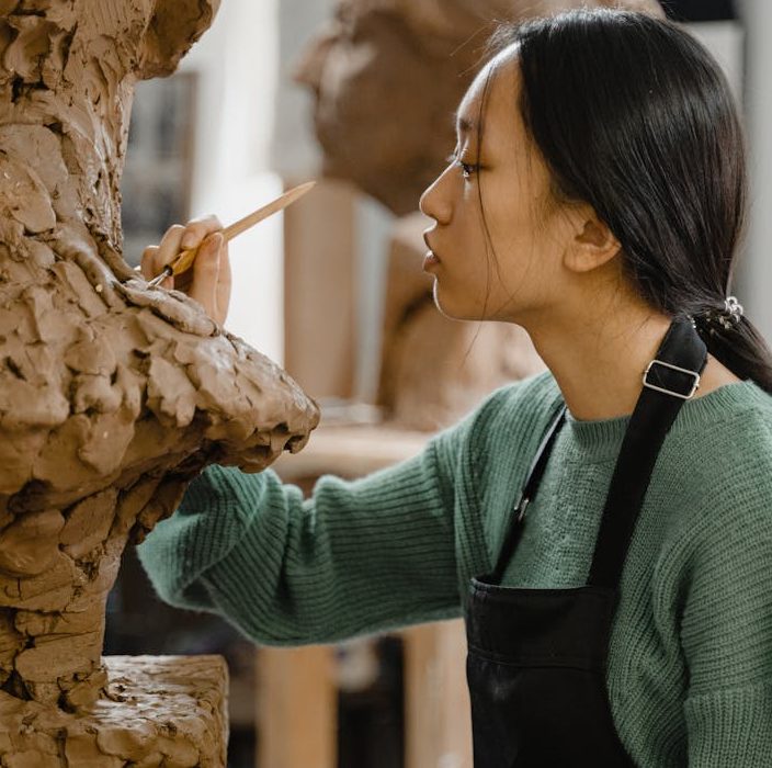 Young sculptor intensely focusing on detailed clay work in an art studio environment.